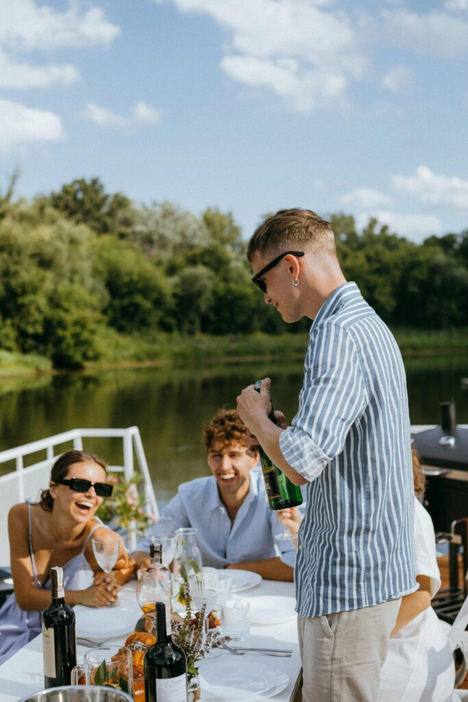 Friends enjoying a sunny outdoor celebration on a yacht with drinks and laughter.